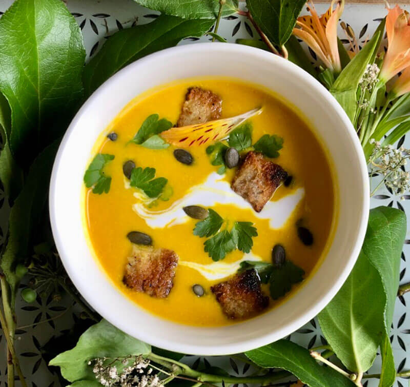 A dish of creamy pumpkin soup on a table designed with Bay leaves done by Dr. Cherine bazzane.