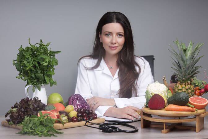 Dr. Cherine seated on her desk surrounded by healthy fruits and vegetables