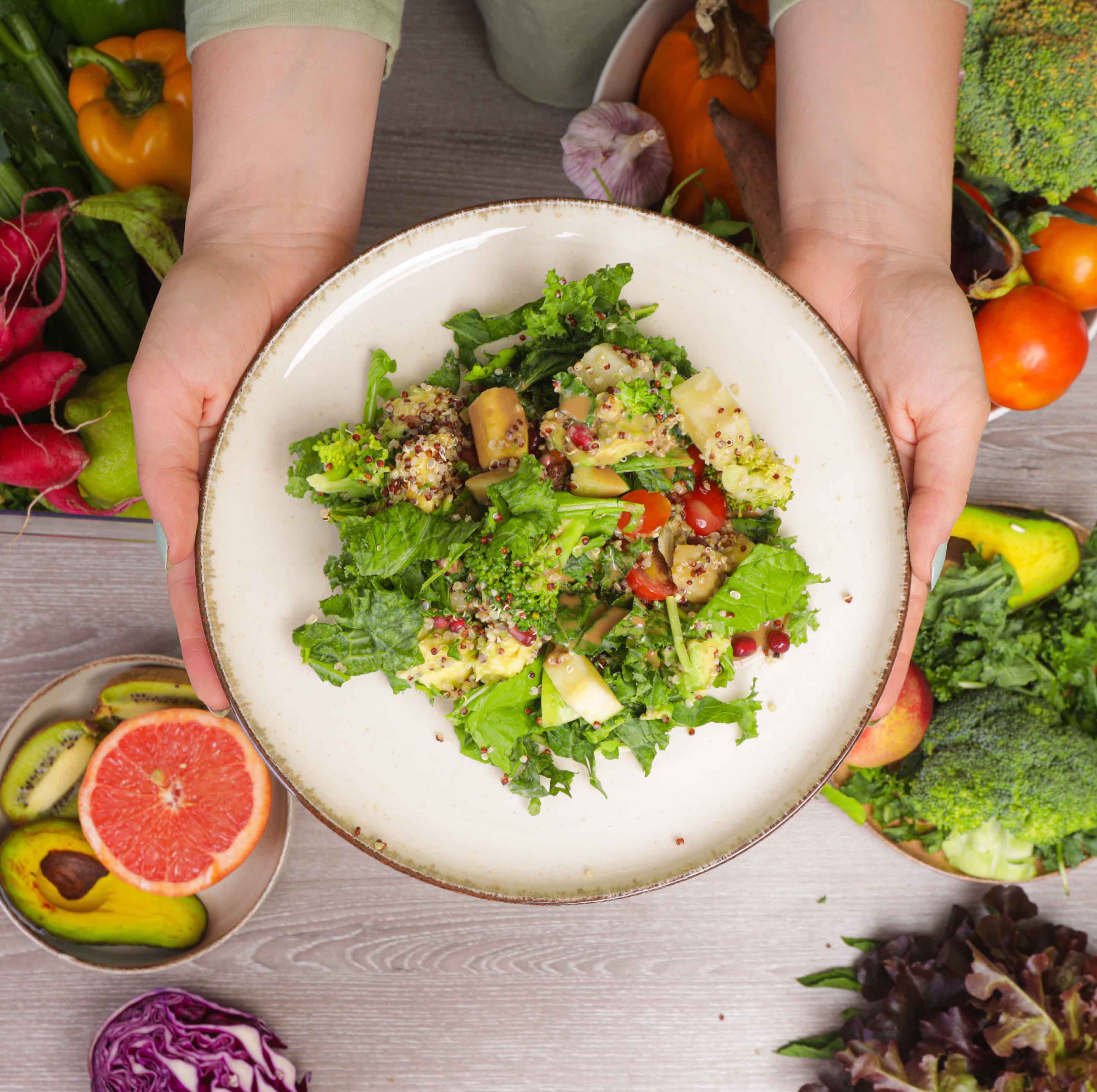 Dr. Cherine holding a healthy salad on a table designed with vegetables and fruit for hormone balance and natural remedies